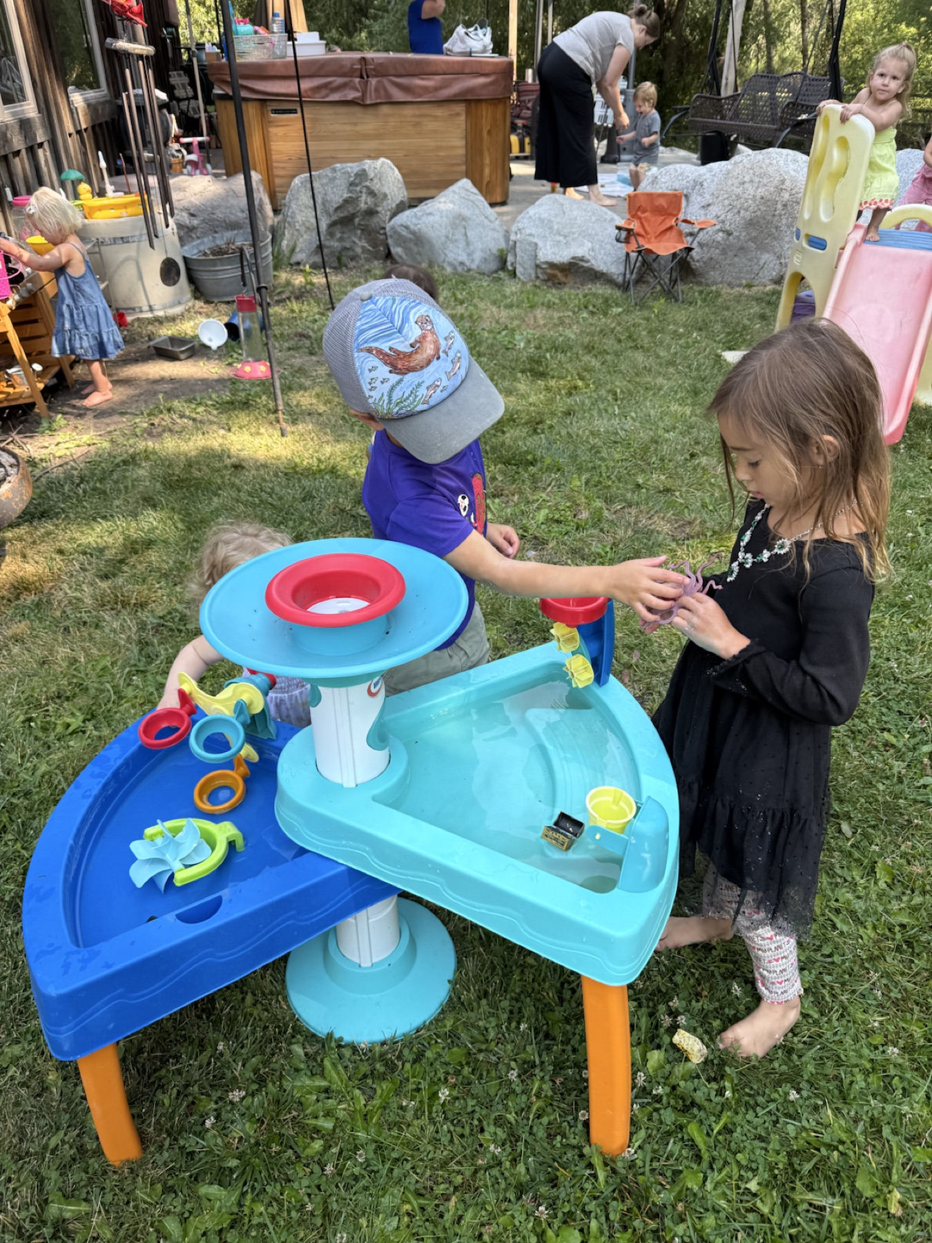 Children sharing toys around an outdoor water table